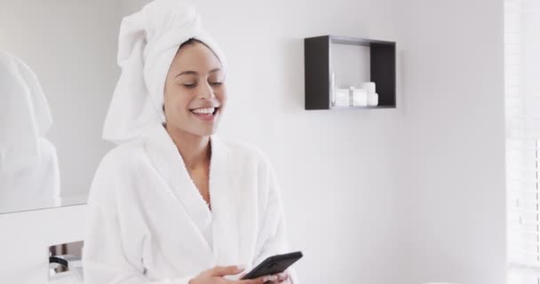 一个快乐的女人头戴毛巾 在浴室里用智能手机 动作缓慢的肖像 生活方式 自我照顾 交流和家庭生活 — 图库视频影像