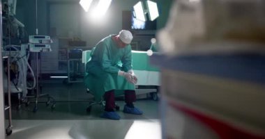 Kafkas erkek cerrah ameliyat önlüğü giyerek hastanede ameliyathanede oturuyor, ağır çekimde. İlaç, sağlık, ameliyat, hastane ve iş, değiştirilmemiş.