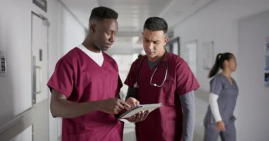 Çeşitli erkek doktorlar işi tartışıyor, hastanenin koridorunda tablet kullanıyorlar, ağır çekimde. Tıp, sağlık, takım çalışması, iletişim, hastane ve çalışma, değiştirilmemiş.