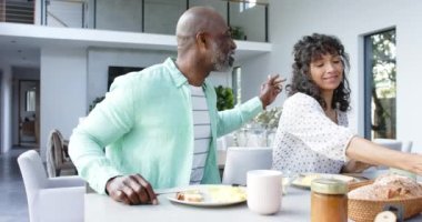 Çift ırklı mutlu çift kahvaltıda omlet yiyor ve mutfakta konuşuyor, ağır çekimde. Ev hayatı, yemek ve yaşam tarzı, değişmemiş..