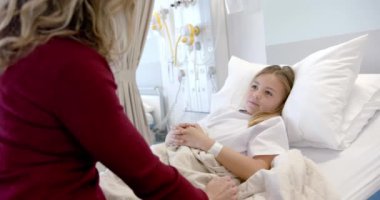 Kafkasyalı anne hasta kızını rahatlatıyor. Hasta yatağında yatıyor, ağır çekimde. Annelik, çocukluk, birliktelik, bakım, sağlık hizmetleri, sağlık ve hastane, değiştirilmemiş.