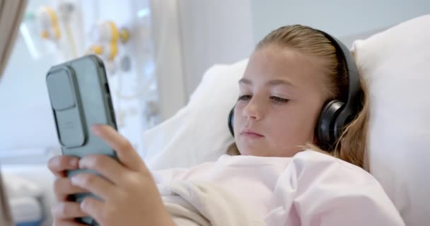Белая Пациентка Лежит Больничной Койке Наушниках Используя Смартфон Замедленная Съемка — стоковое видео
