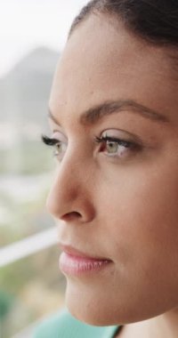 Düşünceli, melez bir kadının pencereden eve bakışının dikey videosu, yavaş çekim. Yaşam tarzı ve ev hayatı, değişmedi..