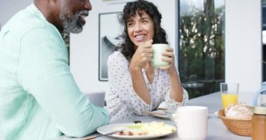 Çift ırklı mutlu çift kahvaltıda omlet yiyor ve mutfakta konuşuyor, ağır çekimde. Ev hayatı, yemek ve yaşam tarzı, değişmemiş..