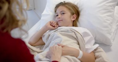 Hasta kızının elini tutan beyaz bir anne hastane yatağında ağır çekimde yatıyor. Annelik, çocukluk, birliktelik, bakım, sağlık hizmetleri, sağlık ve hastane, değiştirilmemiş.