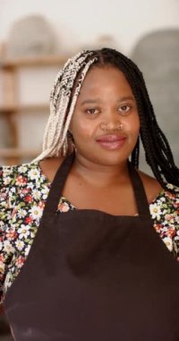 Çömlek atölyesinde durup gülümseyen mutlu Afrikalı Amerikalı kadın, ağır çekimde. Çömlek, seramik, el yapımı, yerel işletme, hobiler ve el işi, değiştirilmemiş.