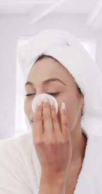 Çift ırklı mutlu bir kadının banyoda temizleyici yüz uygulamasının dikey videosu, yavaş çekim. Yaşam tarzı, özbakım, güzellik ve ev hayatı, değişmemiş..
