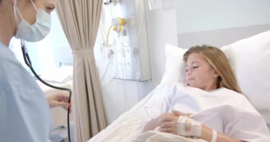 Kafkas maskeli kadın doktor hastane yatağında steteskop kullanıyor, ağır çekimde. Kontrol, hijyen, çocukluk, hastalık, sağlık hizmetleri, sağlık ve hastane, değiştirilmemiş.