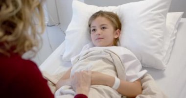 Hasta kızının elini tutan beyaz bir anne hastane yatağında uzanıyor, ağır çekimde. Annelik, çocukluk, birliktelik, bakım, sağlık hizmetleri, sağlık ve hastane, değiştirilmemiş.