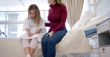 Kafkasyalı mutlu anne hasta kızını rahatlatıyor hastane yatağında oturuyor, fotokopi odası, ağır çekim. Annelik, çocukluk, birliktelik, bakım, sağlık hizmetleri, sağlık ve hastane, değiştirilmemiş.