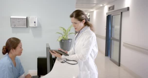 病院受付でタブレットやコンピュータを使った多様な女性医師 コピースペース スローモーション チームワーク コミュニケーション 医療サービス — ストック動画
