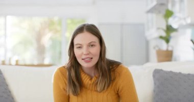 Kanepede oturan mutlu beyaz kadın yavaş çekimde evde video görüşmesi yapıyor. İletişim, yaşam tarzı ve ev hayatı, değişmedi..