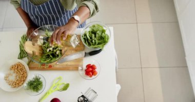 Afrika kökenli Amerikalı son sınıf öğrencisi kadın salatayı güneşli mutfakta hazırlıyor, ağır çekimde. Ev, emeklilik ve yaşlılar yaşam tarzı, ev hayatı, yemek, sağlık, sebze, değişmemiş.