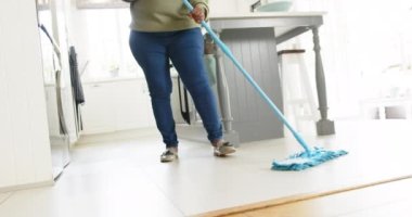 Mutlu Afro-Amerikan son sınıf öğrencisi kadın yerleri temizliyor ve güneşli mutfakta gülümsüyor, ağır çekimde. Ev, emeklilik ve yaşlı yaşam tarzı, ev hayatı, temizlik, değişmemiş.