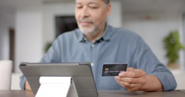 İnternetten ödeme yapmak için kredi kartı ve tablet kullanan mutlu kıdemli çift ırklı adam, yavaş çekim. Çevrimiçi alışveriş, finans, çevrimiçi bankacılık, iletişim, ev hayatı ve yaşlılar yaşam tarzı, değiştirilmemiş.