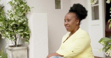Mutlu Afro-Amerikan son sınıf öğrencisi kadın evinin önünde oturmuş gülümsüyor, ağır çekimde..