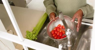 Güneşli mutfakta domates yıkayan Afrikalı Amerikalı son sınıf öğrencisi kadının elleri, ağır çekimde. Ev, emeklilik ve yaşlı yaşam tarzı, ev hayatı, yemek pişirme, değişmemiş.
