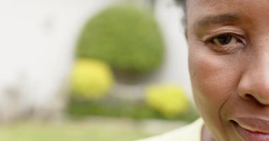 Mutlu Afrikalı Amerikalı son sınıf öğrencisinin yarım yüzü güneşli bahçede gülüyor, ağır çekimde..