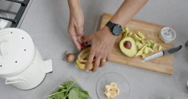 Kıdemli çift ırklı adamın elleri smoothie hazırlıyor, mutfakta gübreleme yapıyor, ağır çekimde. Ekoloji, geri dönüşüm, emeklilik, refah, beslenme, gıda ve sağlıklı yaşam tarzı, değiştirilmemiş.