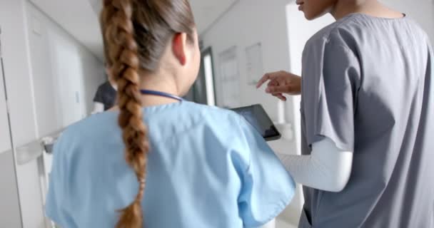Różnorodne Kobiety Lekarzy Omawiających Pracę Pomocą Tabletu Chodzenia Korytarzu Szpitalnym — Wideo stockowe