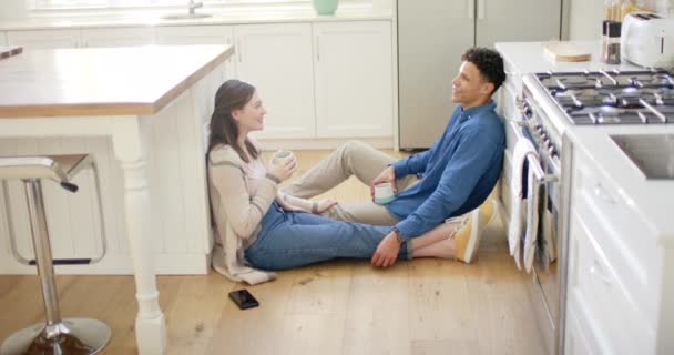 Szczęśliwa Zróżnicowana Para Rozmawiająca Pijąca Kawę Siedząca Podłodze Kuchni Domu — Wideo stockowe
