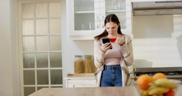 Ευτυχισμένος Καυκάσιος Γυναίκα Χρησιμοποιώντας Smartphone Και Πίνοντας Τσάι Στην Κουζίνα — Αρχείο Βίντεο