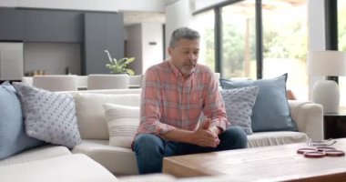 Endişeli kıdemli çift ırklı adam oturma odasında oturup düşünüyor, kopyalama alanı, ağır çekim. Emeklilik, depresyon, akıl sağlığı, yalnızlık, yaşlı yaşam tarzı ve ev hayatı, değişmemiş.