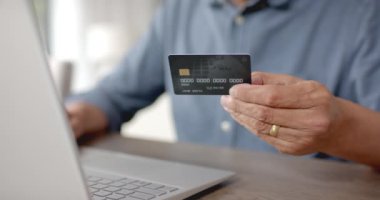 Çevrimiçi ödeme için kredi kartı ve dizüstü bilgisayar kullanan mutlu kıdemli çift ırklı adam, yavaş çekim. Çevrimiçi alışveriş, finans, çevrimiçi bankacılık, iletişim, ev hayatı ve yaşlılar yaşam tarzı, değiştirilmemiş.