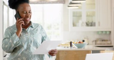 Afrikalı Amerikalı son sınıf öğrencisi evrak işleri yapıyor ve güneşli odada akıllı telefon kullanıyor.. 