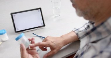 Kıdemli melez adam tablet üzerinde tıbbi video görüntüsü alıyor, uzay ekranını kopyala, yavaş çekim. Teletıp, sağlık hizmetleri, tıbbi danışma, iletişim, ev hayatı ve yaşlılar yaşam tarzı, değiştirilmemiş.