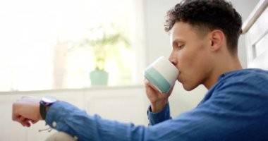 Evde mutfakta yerde ağır çekimde oturan melez bir adam kahve içiyor. Yaşam tarzı ve ev hayatı, değişmedi..