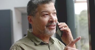 Üst düzey çift ırklı adam akıllı telefondan konuşuyor, pencereden dışarı bakıyor, kopyalama alanı, ağır çekim. İletişim, ev hayatı ve yaşlı yaşam tarzı, değişmedi..
