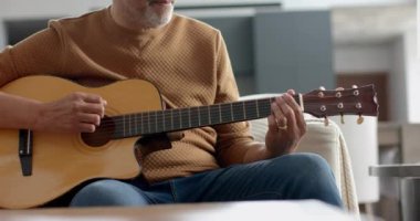 Evde gitar çalarak kanepede oturan yaşlı, çift ırklı bir adam. Müzik, rahatlama, yaratıcılık, hobiler, emeklilik, ev hayatı ve yaşlılar yaşam tarzı, değiştirilmemiş.