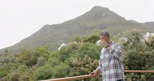 Starszy Dwurasowy Mężczyzna Pijący Kawę Stojący Balkonie Widokiem Góry Przestrzeń — Wideo stockowe