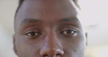 Güneşli oturma odasında gülen mutlu Afro-Amerikalı adamın gözleri, ağır çekimde. Boş zaman ve ev hayatı, duygu, mutluluk, refah, değişmemiş.
