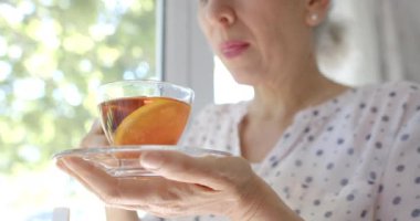 Düşünceli üst düzey çift ırklı kadın. Evinin penceresinde çay içiyor. Ağır çekimde. Ev hayatı, emeklilik, içki ve yaşam tarzı, değişmemiş..