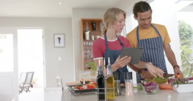 Mutlu çift taze sebzeler hazırlıyor ve mutfakta tablet kullanıyorlar, ağır çekimde. Sağlıklı, diyet, ev hayatı, yemek, yemek, teknoloji ve yaşam tarzı, değişmemiş.