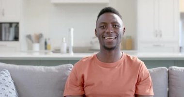 Mutlu Afro-Amerikalı adam güneşli oturma odasında video çekiyor, ağır çekimde. Ev, ev hayatı, yaşam tarzı, refah, iletişim, teknoloji, değişmemiş..