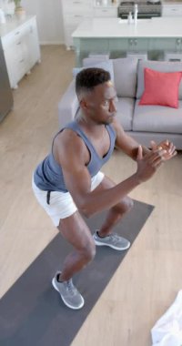 Odaklanmış Afro-Amerikan adam güneşli oturma odasında ağır çekimde çömeliyor. Ev, egzersiz, fitness ve sağlıklı yaşam tarzı, değişmemiş..