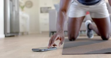 Afrika kökenli Amerikalı bir adam oturma odasında akıllı telefon kullanarak dağcılık yapıyor, ağır çekimde. Ev, egzersiz, fitness ve sağlıklı yaşam tarzı, iletişim, değişmemiş.