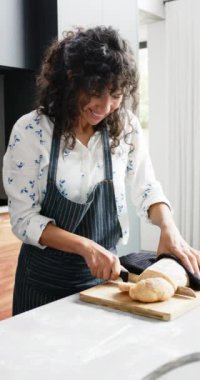 Kafkas kadının evde taze ekmek dilimlediği dikey video, yavaş çekim. Pişirme, pişirme, yemek, ev hayatı ve yaşam tarzı, değiştirilmemiş.