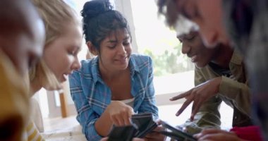 Akıllı telefonlar kullanan ve evdeki halının üzerinde ağır çekimde uzanan mutlu genç arkadaş grubu. Gen Z, arkadaşlık, takılma, teknoloji ve yaşam tarzı, değişmemiş..