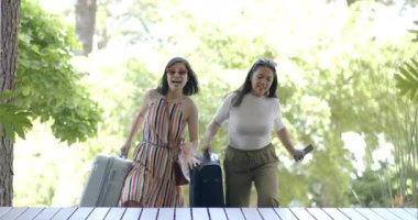 Bavulları ve akıllı telefonları olan mutlu Asyalı bayan arkadaşlar evlerinin merdivenlerinde ağır çekimde yürüyorlar. Yaz, eve dönüş, seyahat, arkadaşlık, iletişim, değişmemiş.