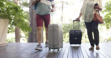 Çeşitli yaşlı çiftler valizleriyle güneşli bir eve doğru yürüyorlar. Emeklilik, dinlenme, seyahat, inşaat ve doğa konsepti, değiştirilmemiş..