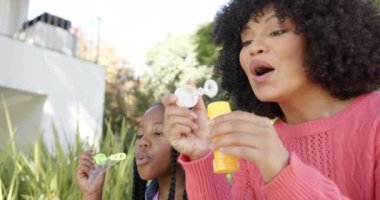 Mutlu Afro-Amerikan annesi ve kızı bahçede köpük üflüyor, ağır çekimde. Ev hayatı, doğa ve yaşam tarzı, değişmedi..