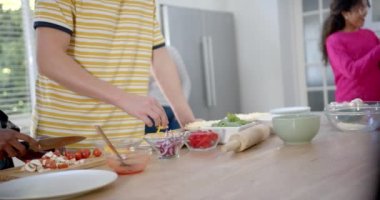 Akıllı telefon kullanan ve mutfakta pizza yapan mutlu bir grup genç arkadaş, yavaş çekim. Gen z, arkadaşlık, takılma, yemek ve yaşam tarzı, değişmemiş.