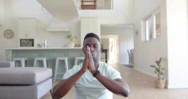 Odaklanmış Afrikalı Amerikalı adam güneşli oturma odasında yoga meditasyonu yapıyor, ağır çekimde. Ev, refah, zindelik ve sağlıklı yaşam tarzı, değişmemiş..
