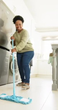 Mutlu Afro-Amerikan son sınıf öğrencisi kadın güneşli mutfakta yerleri temizliyor, ağır çekimde. Ev, emeklilik ve yaşlı yaşam tarzı, ev hayatı, temizlik, değişmemiş.