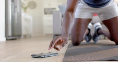 Afrika kökenli Amerikalı bir adam oturma odasında akıllı telefon kullanarak dağcılık yapıyor, ağır çekimde. Ev, egzersiz, fitness ve sağlıklı yaşam tarzı, iletişim, değişmemiş.