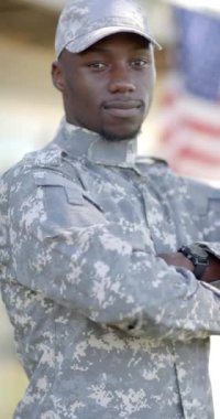 Güneşli bir günde arka planında bayrak olan mutlu Afro-Amerikan erkek askeri, ağır çekimde. Askerlik, ordu, vatanseverlik, değişmemiş.